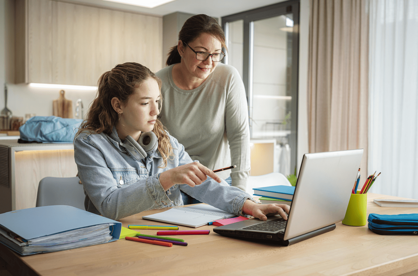 A parent and teenager looking at a laptop together at the kitchen table