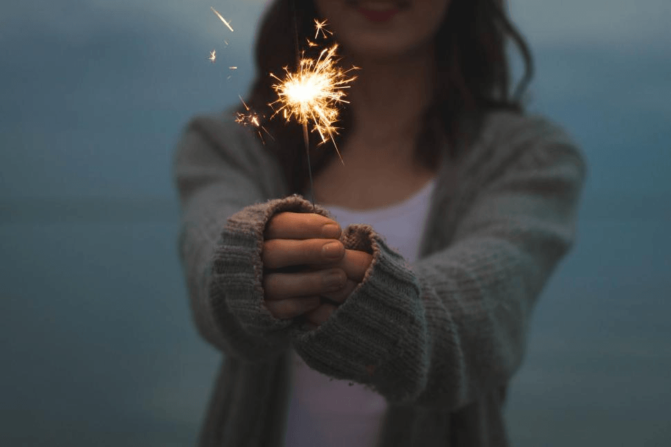 A young person holding a lit sparkler at dusk