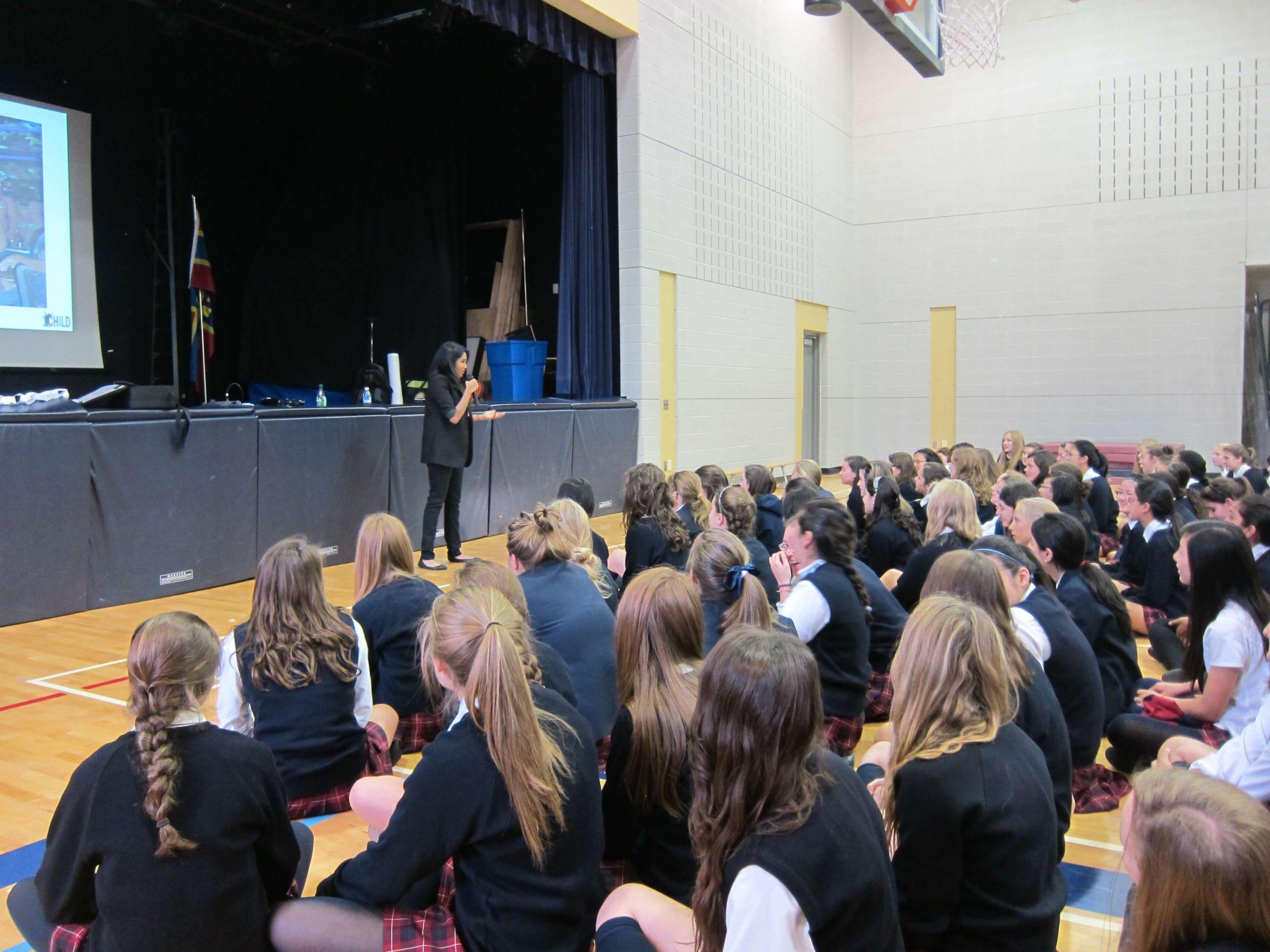 A OneChild educator speaking to a school assembly of seated students